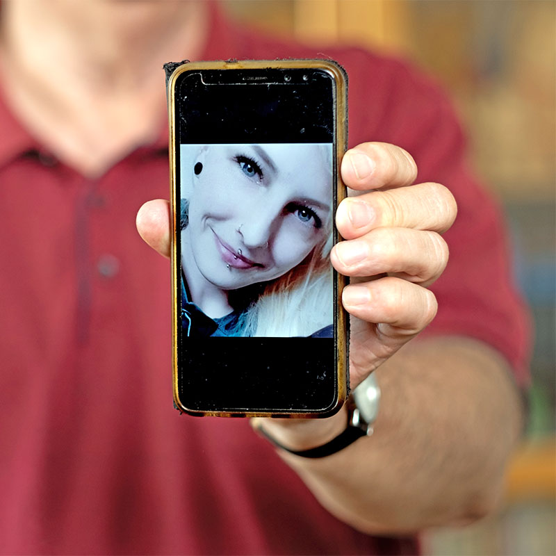 Mann hält sein Smartphone in die Kamera, auf dem das Bild seiner verstorbenen Tochter zu sehen ist