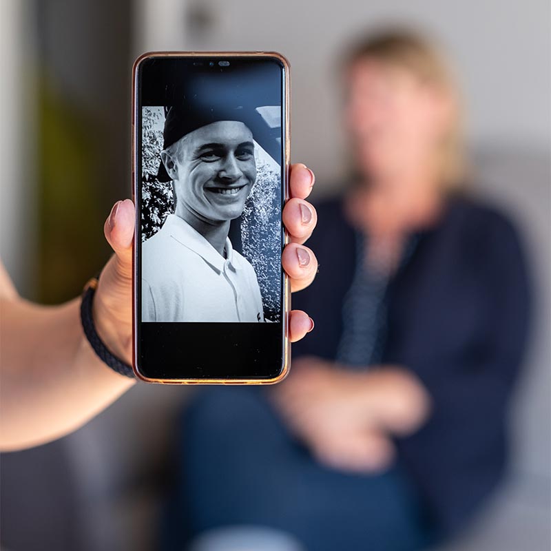 Eine Hand hält ein Smartphone in die Kamera, das das Bild eines jungen Mannes zeigt
