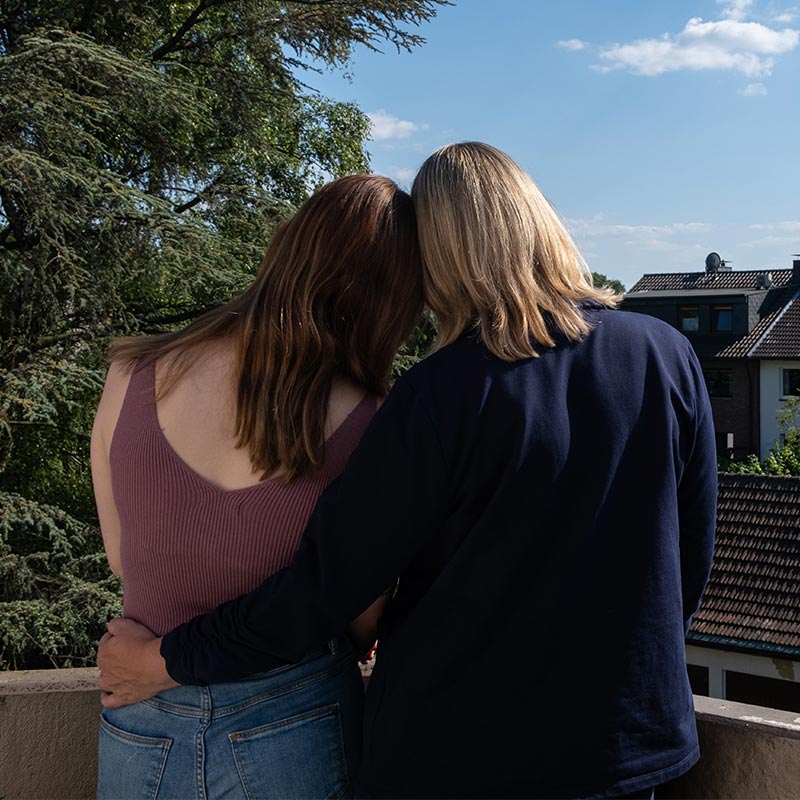 Mutter und Tochter lehnen sich aneinander an und schauen auf dem Balkon in die Ferne